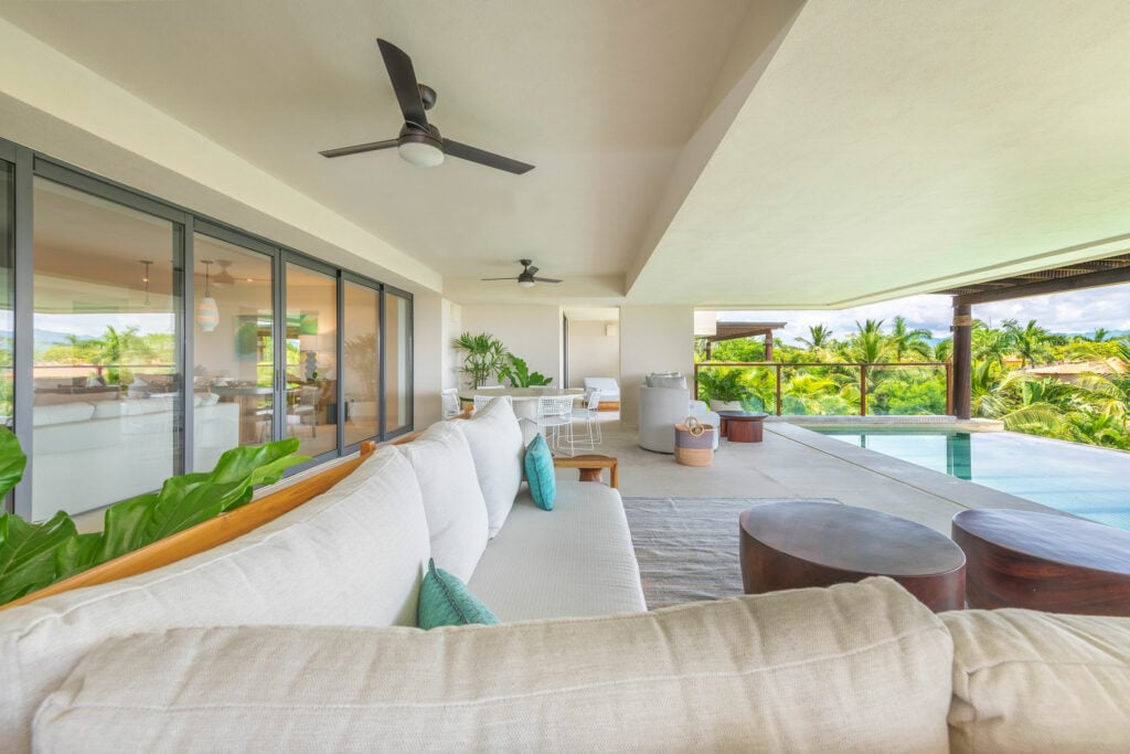 Condo Nova covered terrace with a white sectional, round wood tables and pool — Punta Mita Nayarit, Mexico