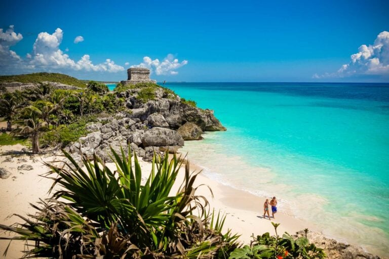 Stone coastal ruins above a white beach and turquoise water