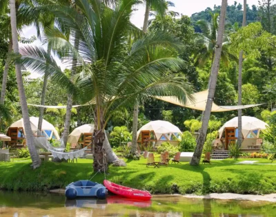 Santuario Yelapa México Wellness & Yoga Retreat: Domos geodésicos, palmeras, río con botes, hamaca y exuberantes colinas boscosas.