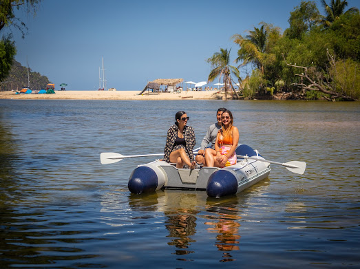 Three people smile on a raft at Santuario Yelapa Mexico Wellness & Yoga Retreat, surrounded by lush beach scenery.