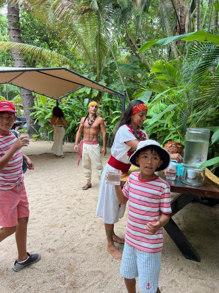 Children with drinks and adults in traditional dress gather at Santuario Yelapa Mexico Wellness & Yoga Retreat's lush grounds.