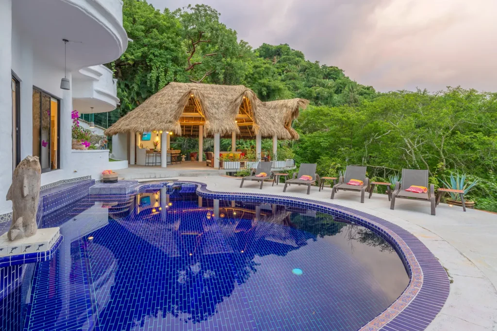 Villa Viaje curved blue-tile pool facing the thatched pavilion at dusk — Puerto Vallarta, Mexico