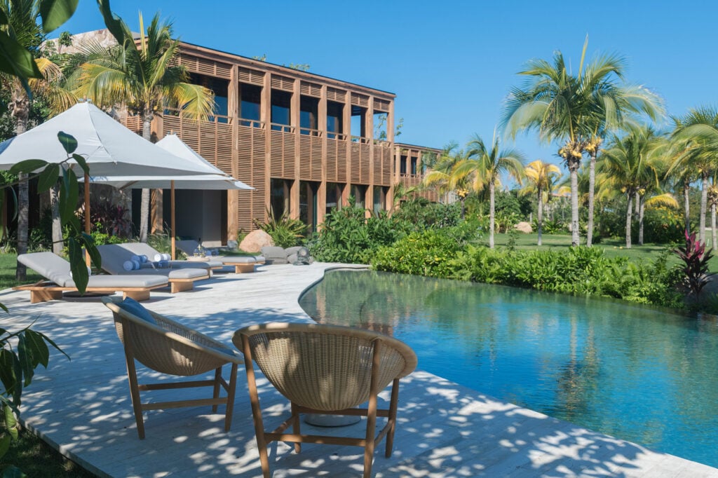 Casa Balena two woven chairs at the pool's edge below the timber-clad wing — Punta Mita, Mexico