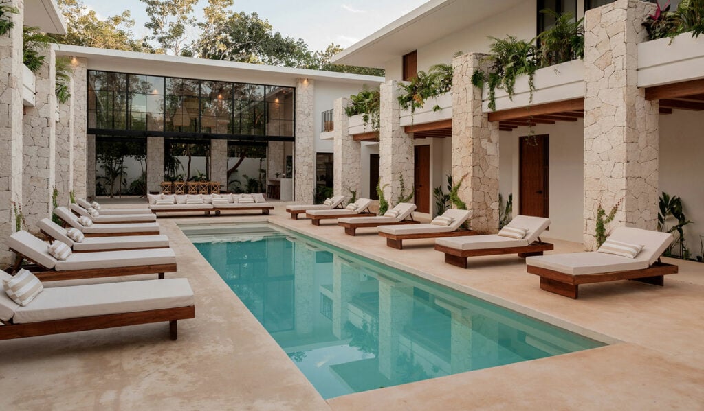 Hacienda Babylon loungers ranged along the courtyard pool below the stone arcade — Tulum, Mexico