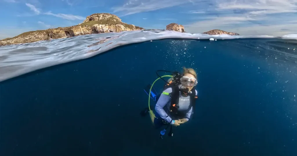 A diver just below the surface with the rocky islands on the horizon behind