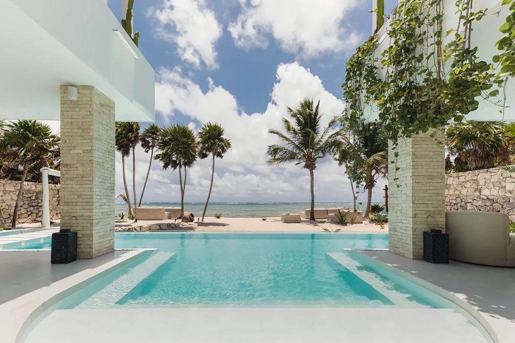 Studio 54 pool framed by two stone columns, palm trees and the ocean — Tulum, Mexico