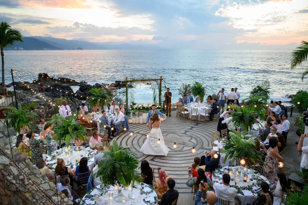 A reception under way on the stepped beachfront terraces at Casa Karma at dusk, the sun going down behind the bay