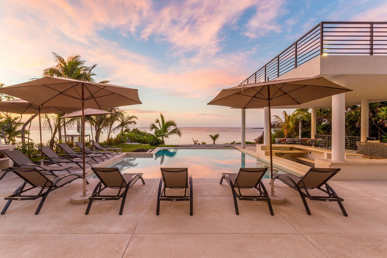 Casa Milah poolside dining tables beneath umbrellas at dusk — Half Moon Bay, Akumal, Mexico