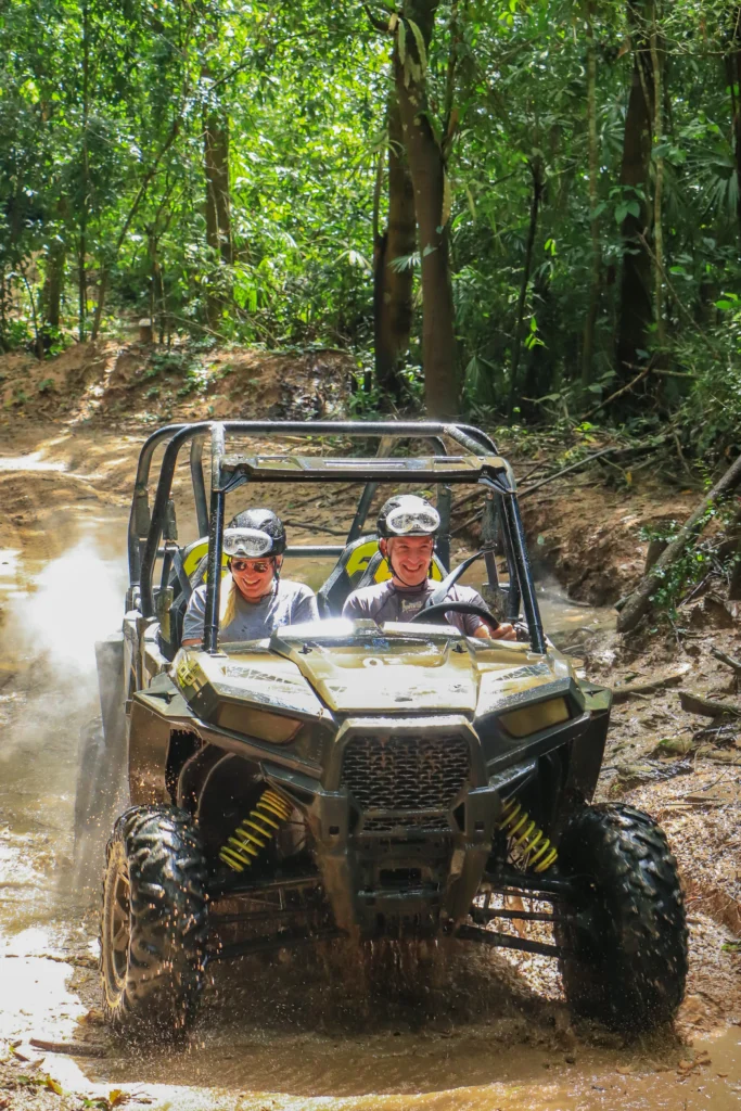 Seen head-on, a buggy climbs a wet rutted track with tall green jungle closing in above.