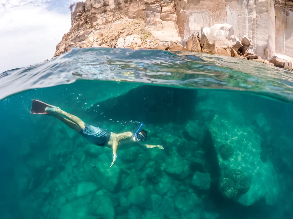 A split shot showing a snorkeller underwater and the cliffs above the surface.