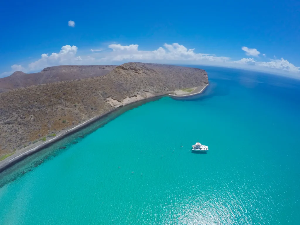 A small boat sits on turquoise water beside a pale sandbar seen from above.