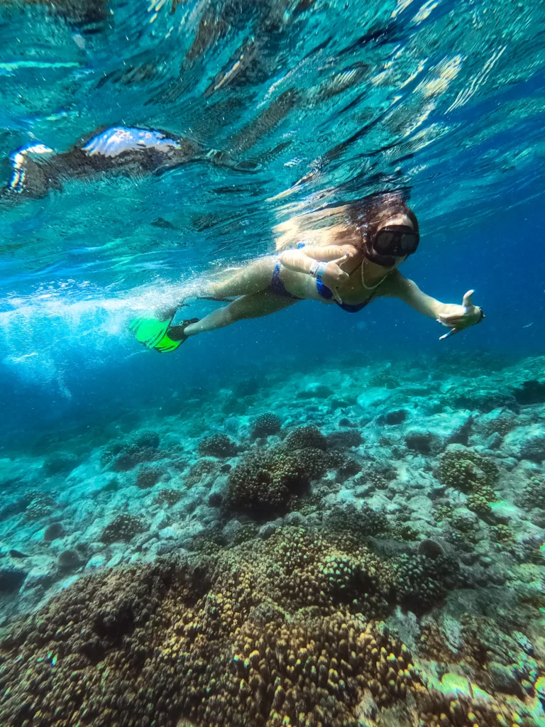 A snorkeller swims over a rocky reef in clear blue-green water.