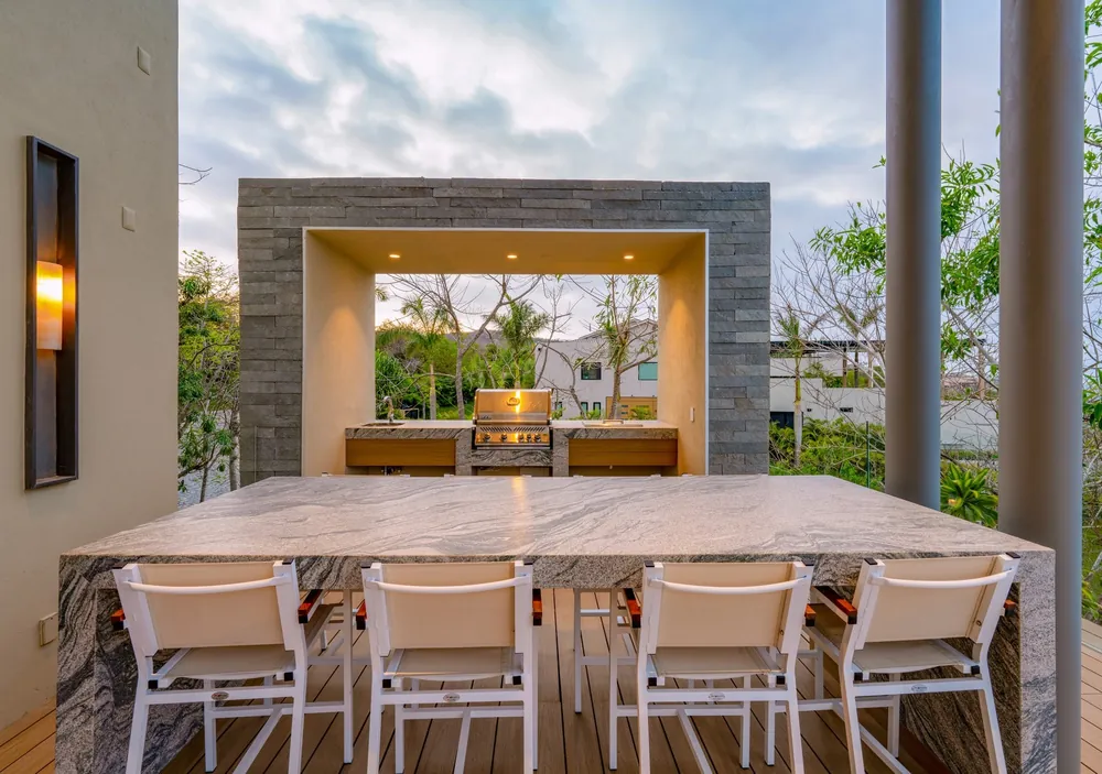 A long table for twelve under a stone-framed covered terrace, a grill at the back