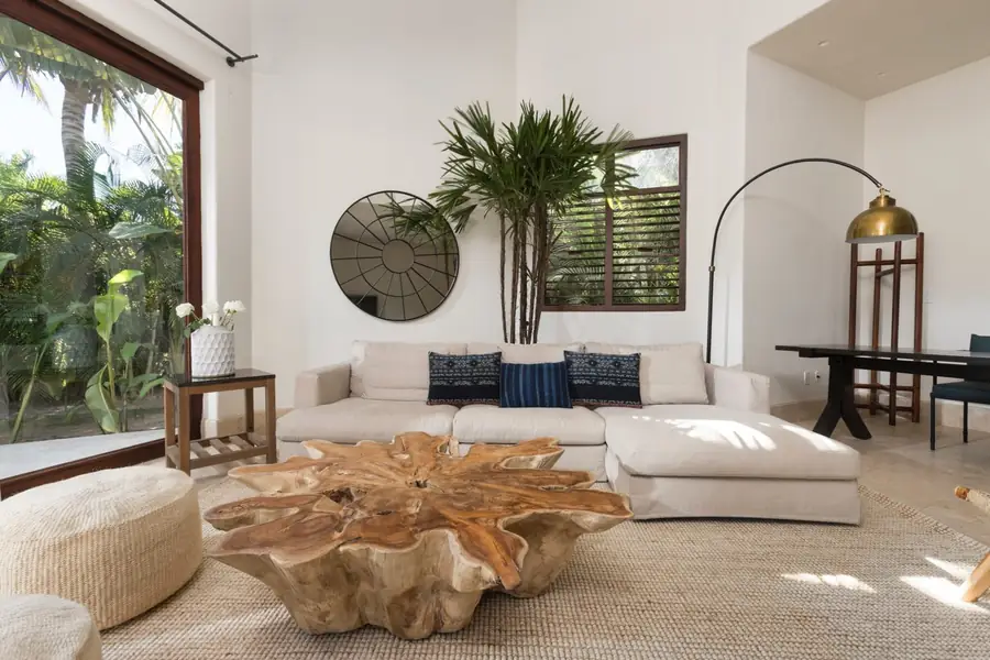 A white living room with a carved wood table and garden windows at Casa La Vida, Punta Mita