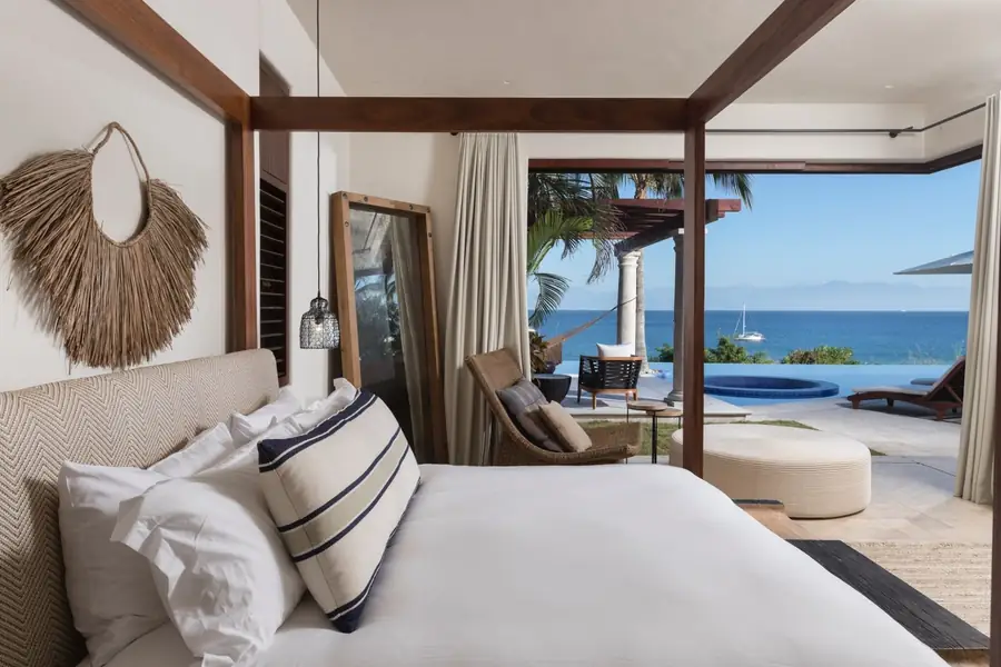 A bedroom with a fringed headboard and the ocean through glass doors at Casa La Vida, Punta Mita