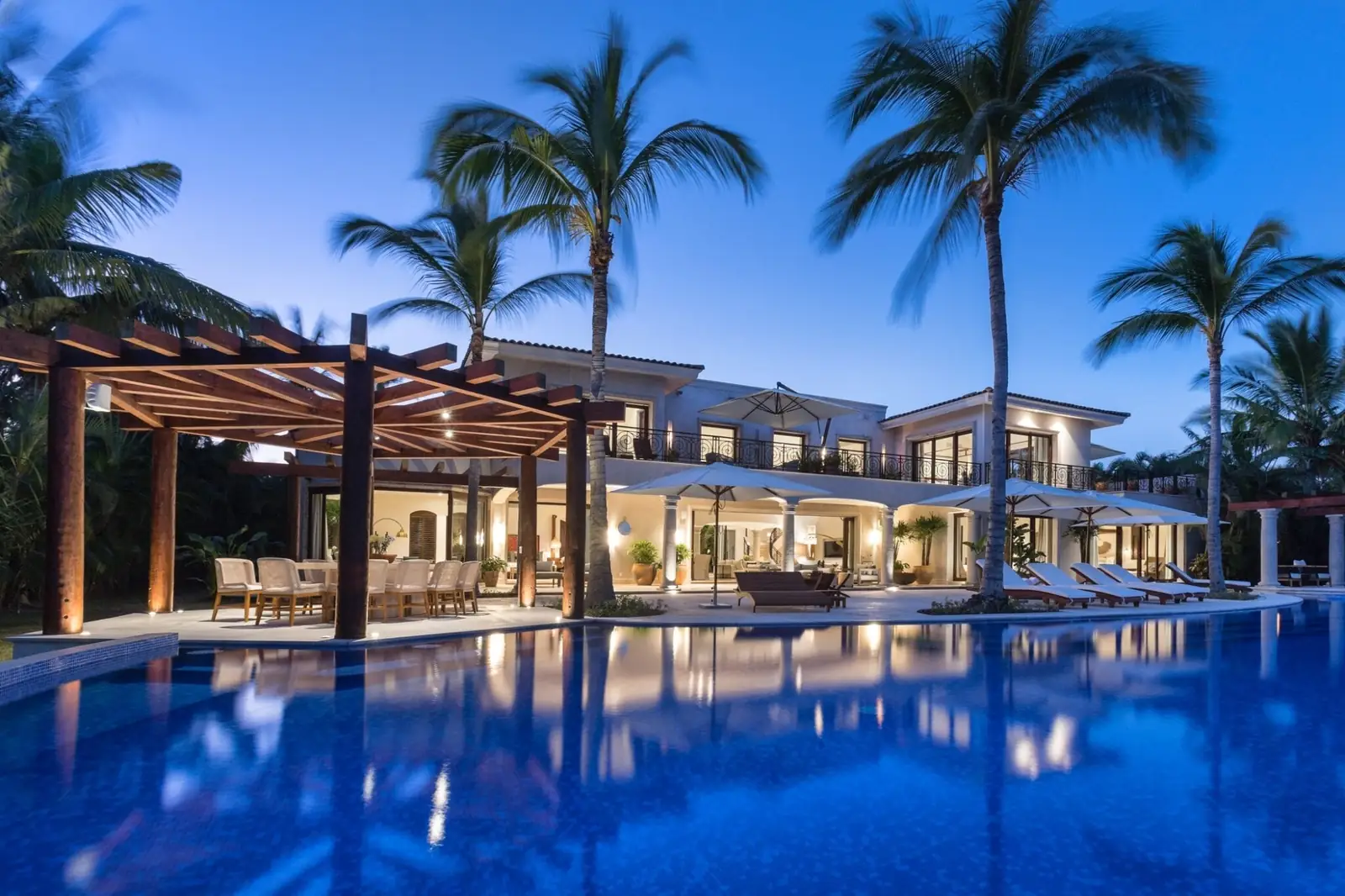 Casa La Vida, a six-bedroom villa in La Punta Estates, Punta Mita, at dusk: lit terraces reflected in a long palm-lined pool
