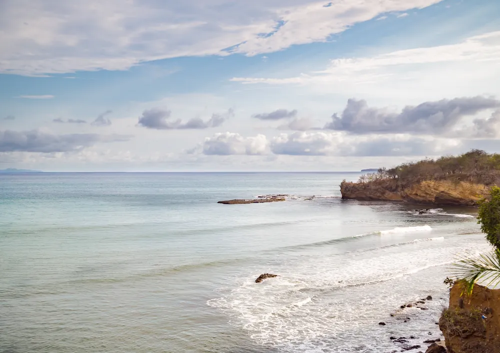 A quiet sandy beach with small waves and a rocky headland under a soft sky, seen from Casa Tres Reinas, Punta de Mita