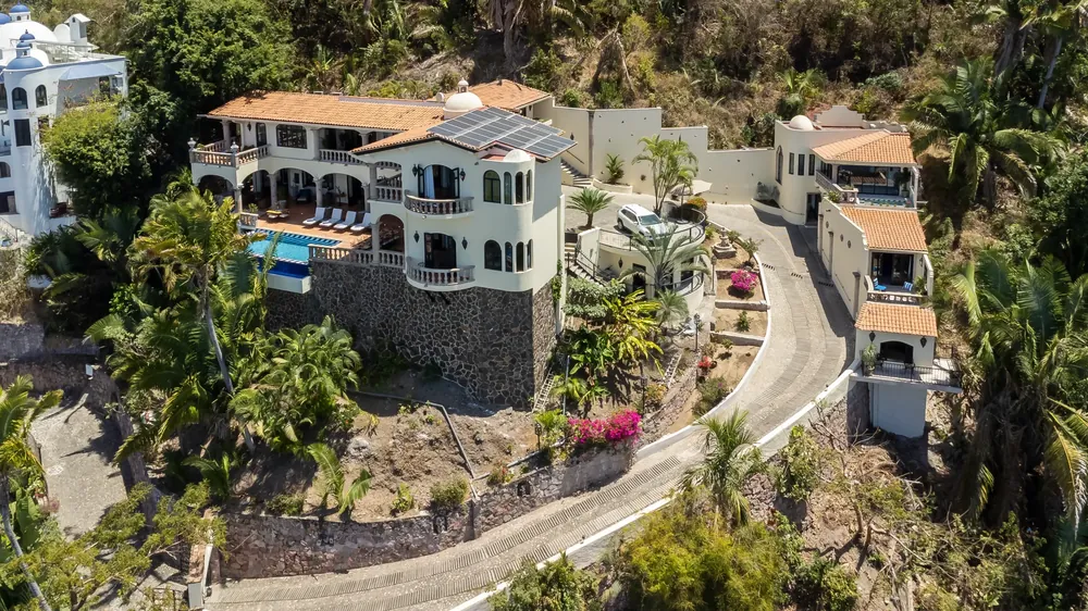 Aerial view of a white hacienda-style villa with a dome and a pool on a jungle hillside, with a winding stone drive and neighbouring houses, Conchas Chinas