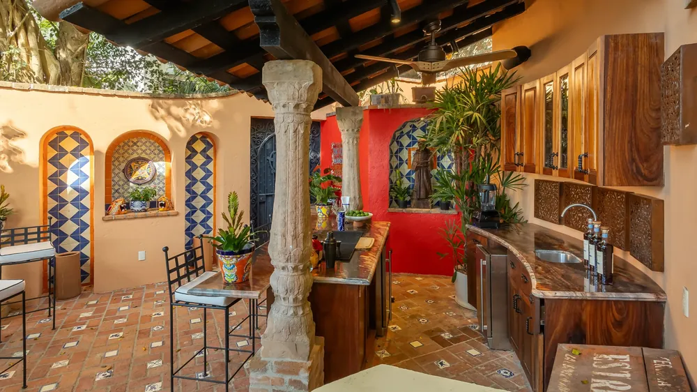 An open covered kitchen with carved stone columns, blue-and-white tile arches, a red wall and a granite bar, Hacienda de los Santos, Puerto Vallarta