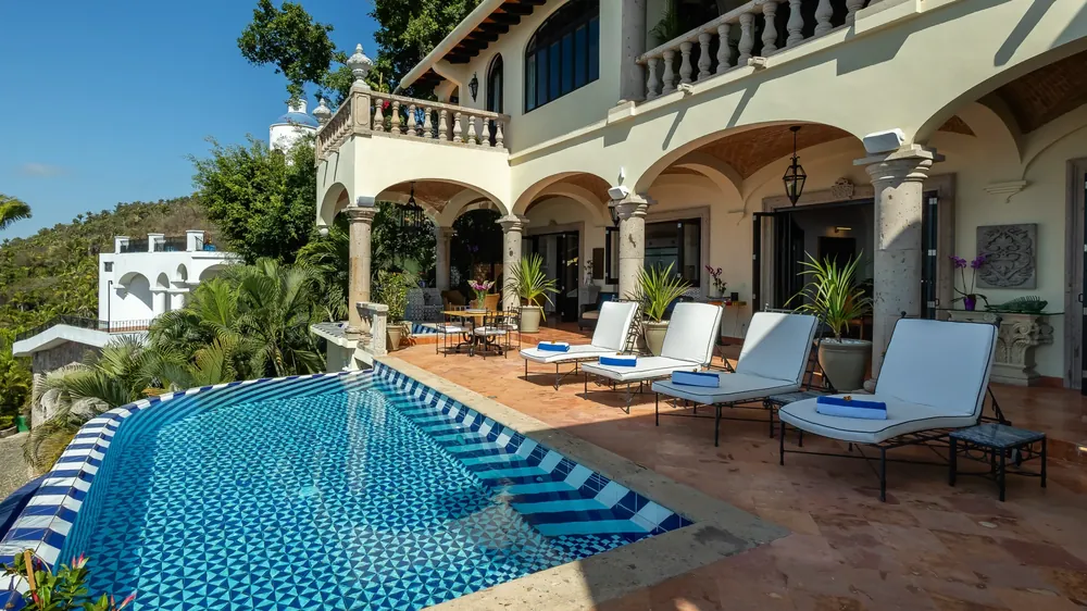 A blue-and-white tiled pool with loungers below the arched, balustraded facade of a hacienda-style villa, Hacienda de los Santos, Puerto Vallarta