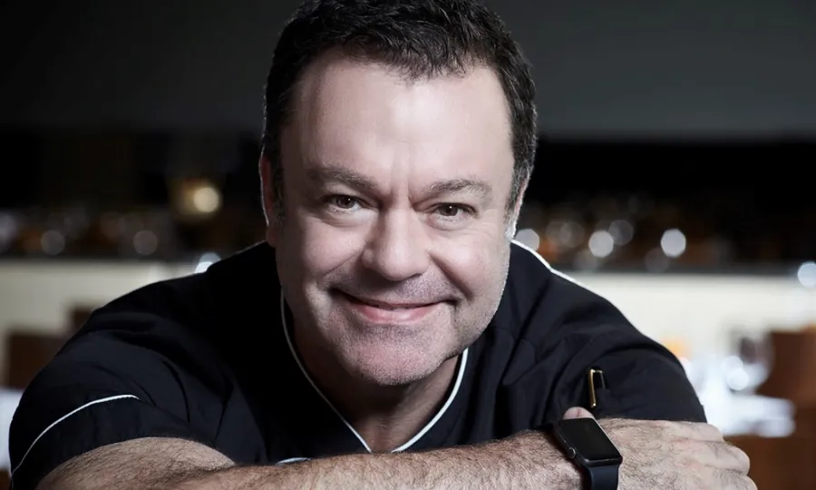Abraham Salum smiling, arms folded, in a black chef's jacket in a dim dining room