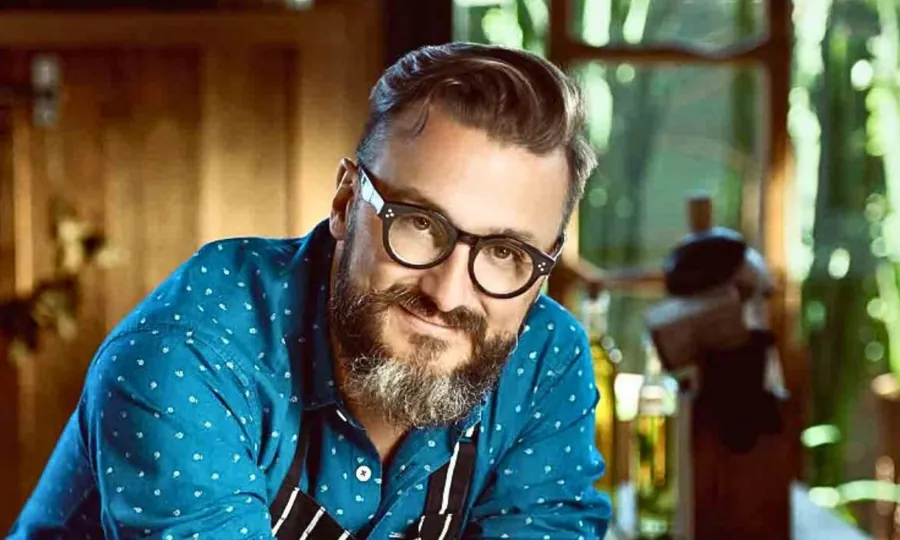 Fernando Trocca in glasses and a patterned shirt, leaning on a counter with greenery behind