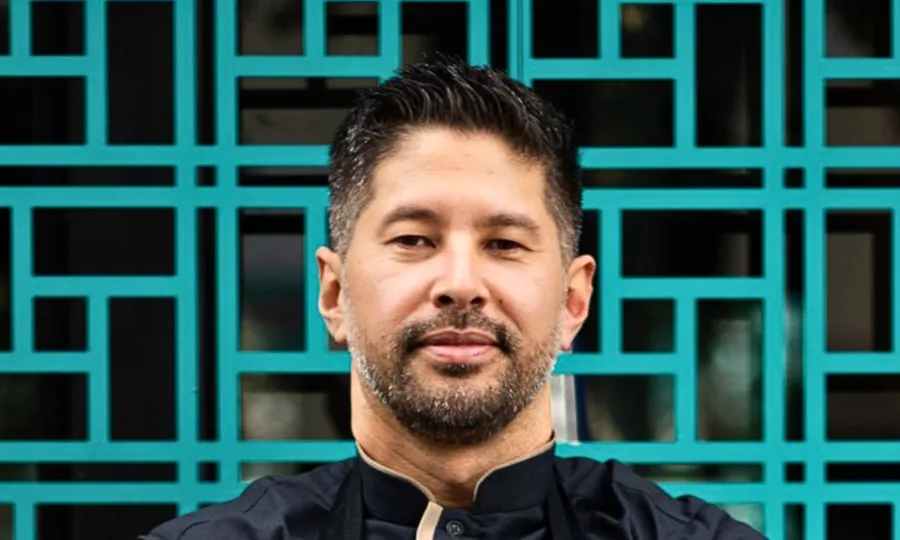 Kazuo Harada in a dark chef's jacket, arms folded, in front of a teal lattice screen