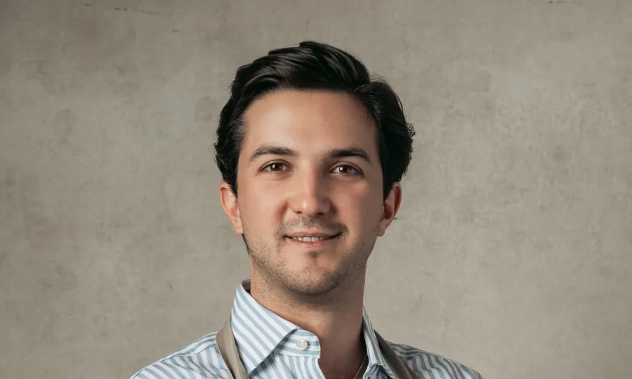 Rodrigo Cardenas in a striped shirt and apron against a plain grey wall