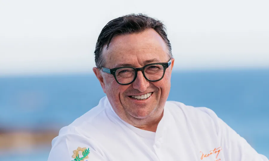Xavier Salomon in glasses and a white chef's jacket, arms folded, with the sea behind him