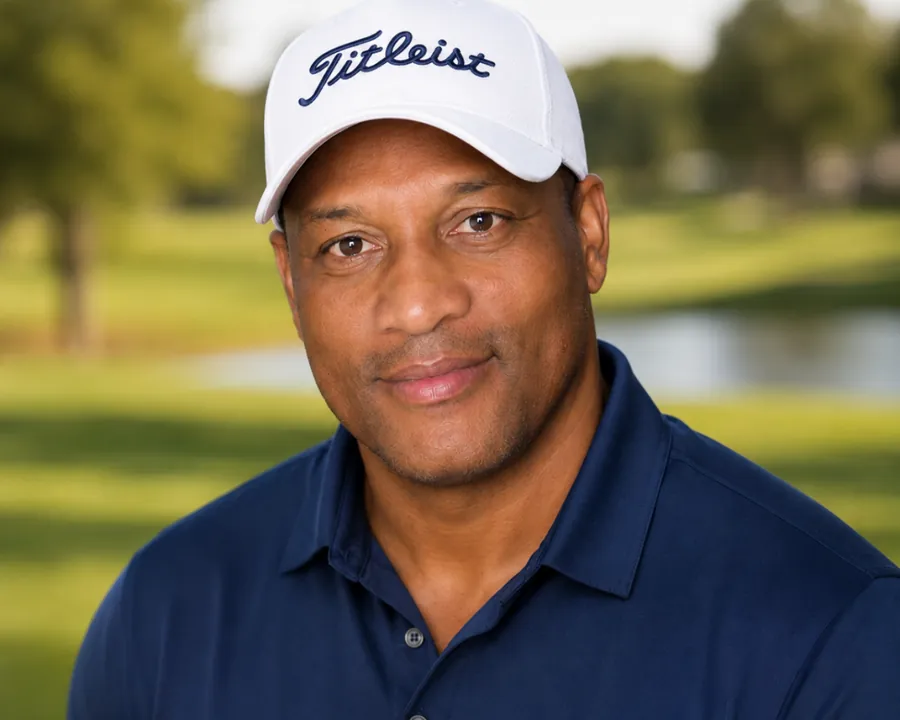 Larry Brown in a white cap and navy polo, smiling, with trees and a lake behind him