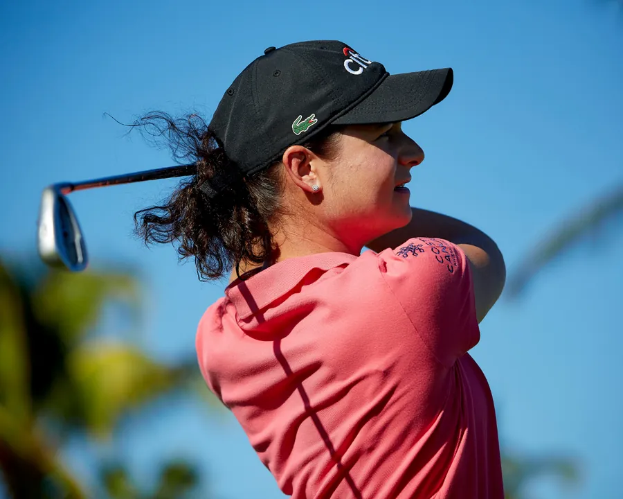 Lorena Ochoa in a red shirt and cap finishing a golf swing against a blue sky
