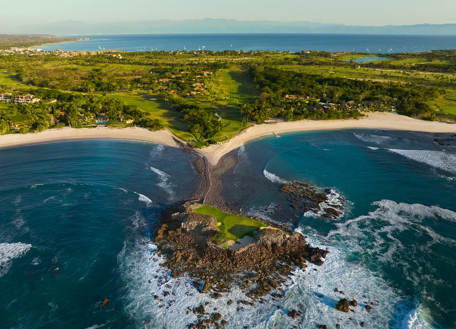 Aerial view from over the sea of the Tail of the Whale island green, with turquoise water, white surf, the beach and the Pacífico course behind, Punta Mita