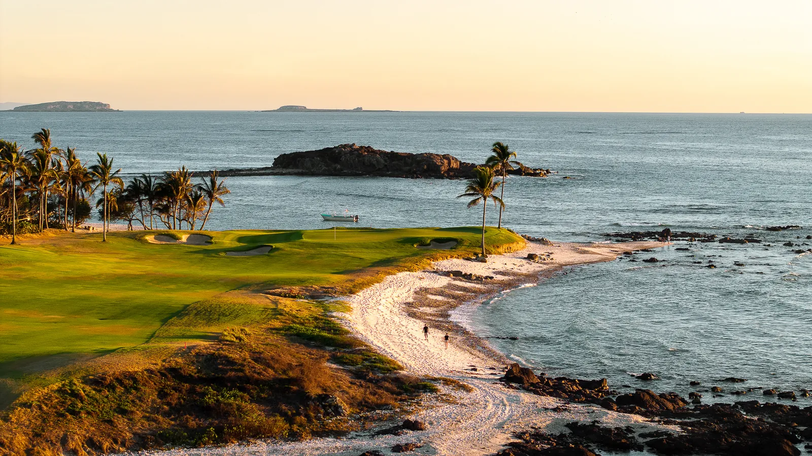 A golf green beside the beach at dusk with palm trees, the rocky Tail of the Whale island just offshore and the Marietas Islands on the horizon, Punta Mita