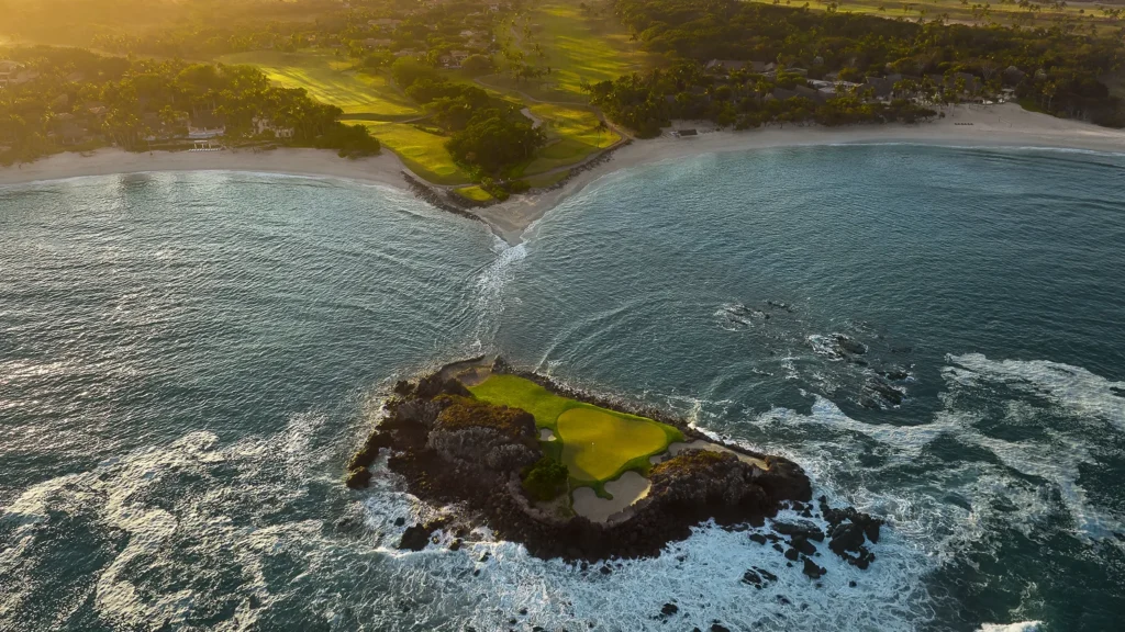 Aerial view at sunrise of the Tail of the Whale, a golf green on a rock island off the beach, with the Pacífico fairways and the bay behind, Punta Mita