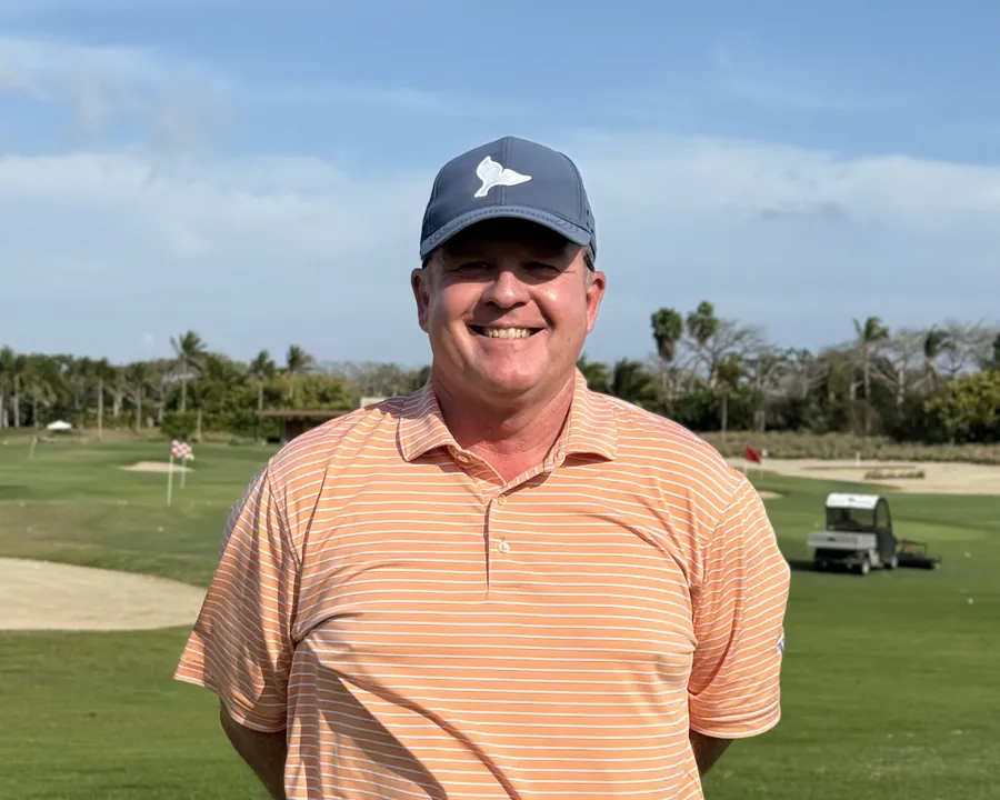 Virgil Herring in an orange polo and cap on a driving range, palms behind