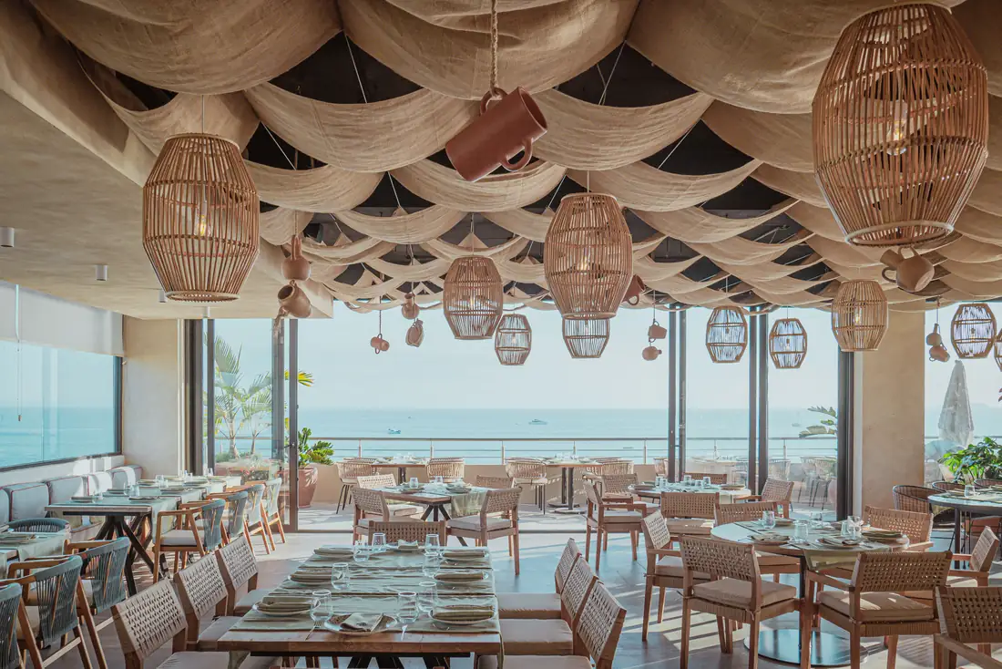 Hoja Santa's dining room under woven lamps, with the bay through the windows, Punta de Mita