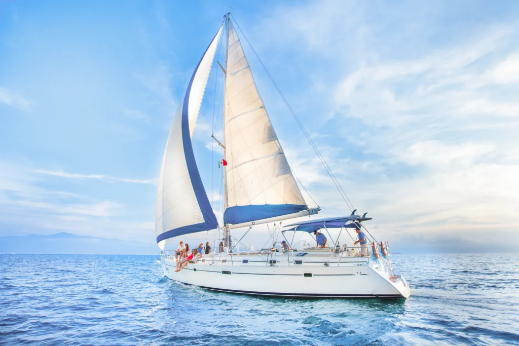 A yacht leans into the wind under two white sails on open water below a tall cloudy sky.