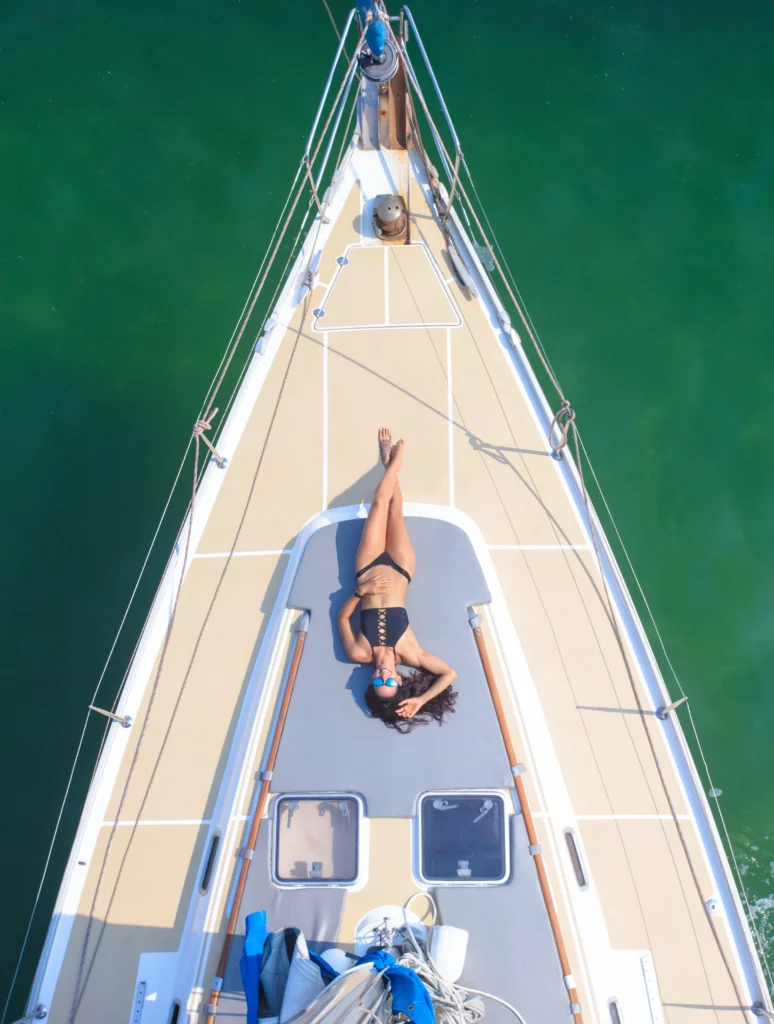 An aerial view straight down the bow of a sailing boat with a guest on the foredeck.