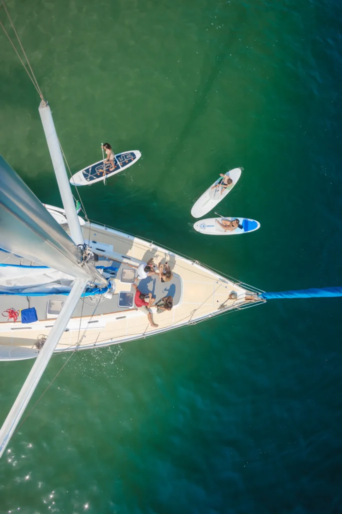 An aerial view of a sailing boat at anchor with paddleboards in the water behind it.
