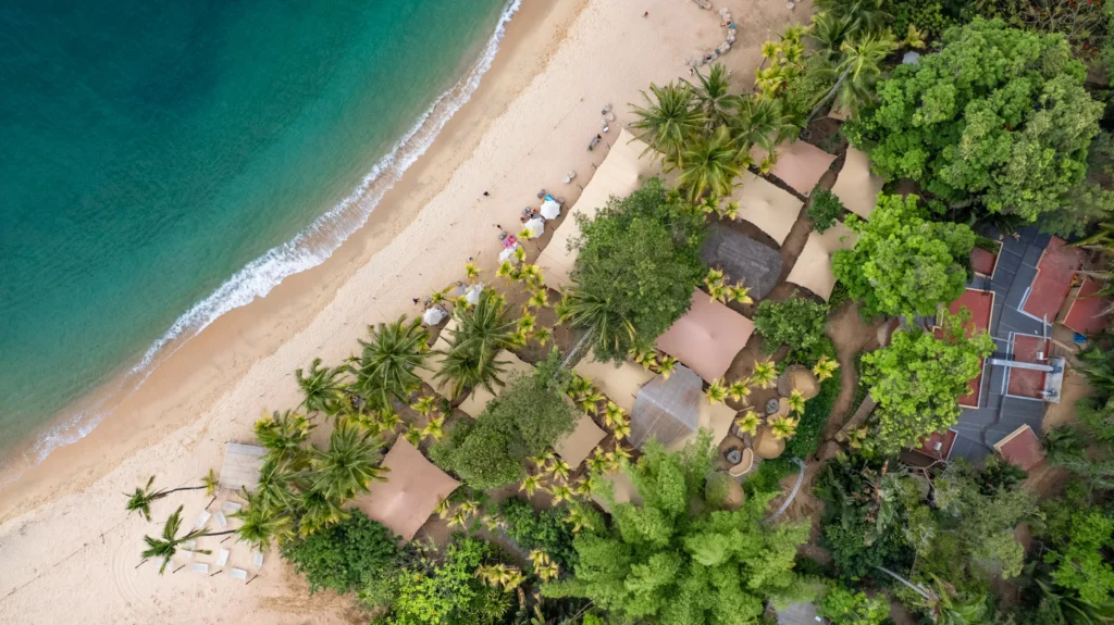 From above, thatched palapas line a curving sand beach where jungle meets clear green water.