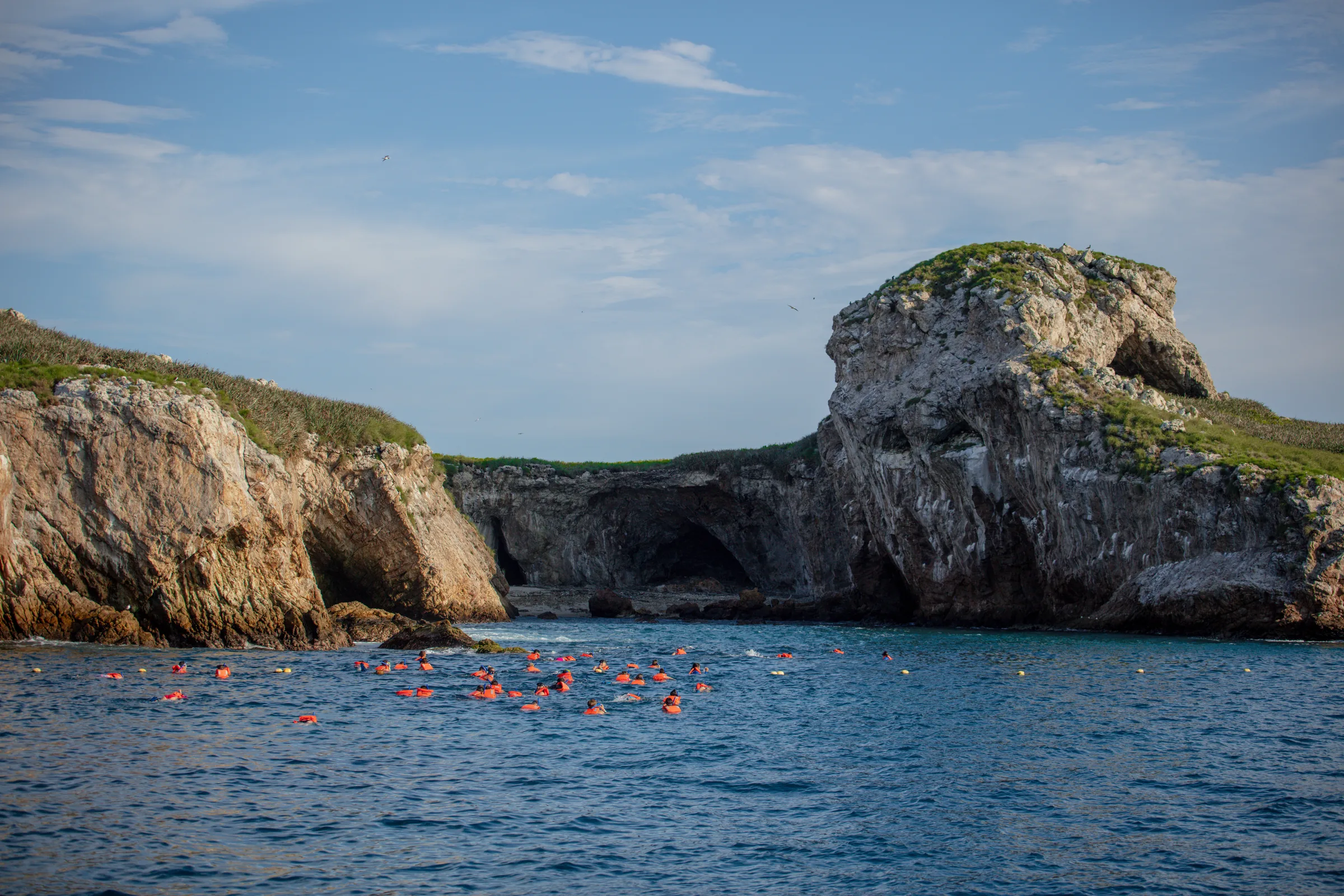A weathered rock arch rises from deep blue water against a bright sky on a bare island.