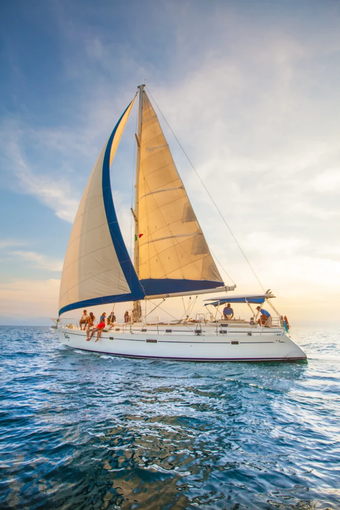 Seen from low down, a tall sail rises above a white hull cutting through choppy blue water.