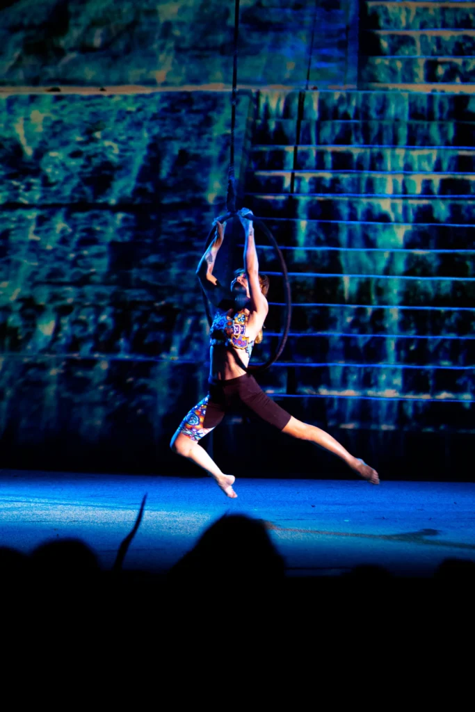 A dancer suspended in mid-air against a stone pyramid washed in blue and green light.