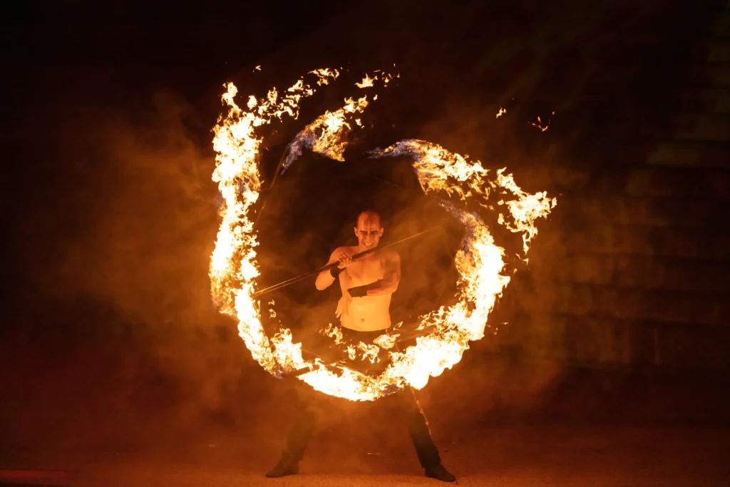 A fire dancer moves inside a spinning ring of flame on the open-air stage at night.