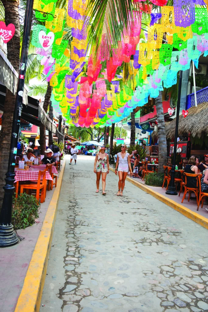 Dense rows of bright cut paper flags hang above a narrow cobbled lane lined with cafes.