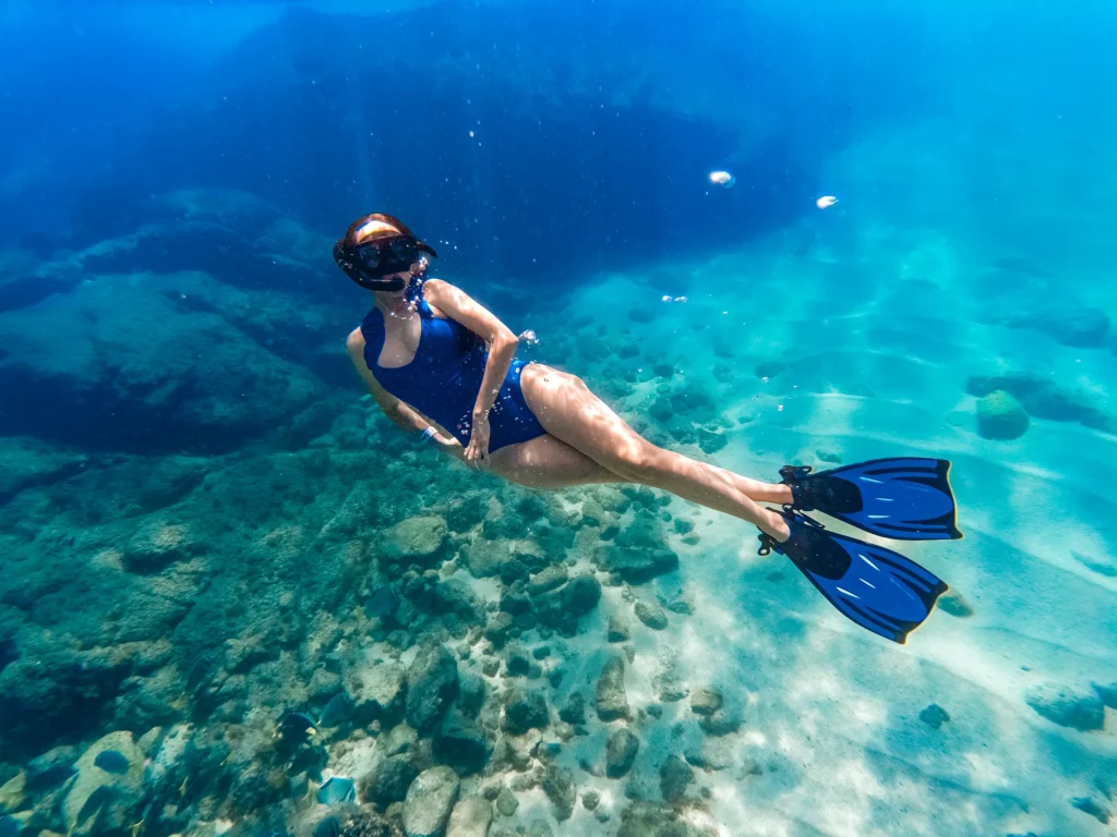 A snorkeller swims over a bright turquoise reef in clear shallow water.