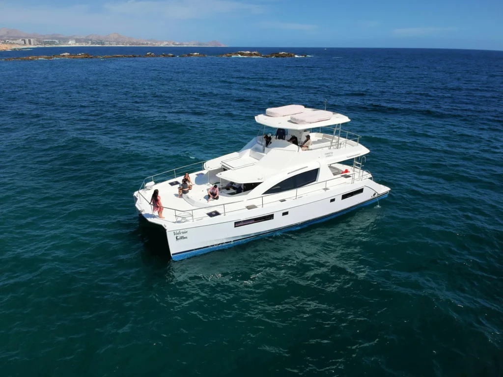 A white power catamaran lies at anchor off a dry rocky coastline.