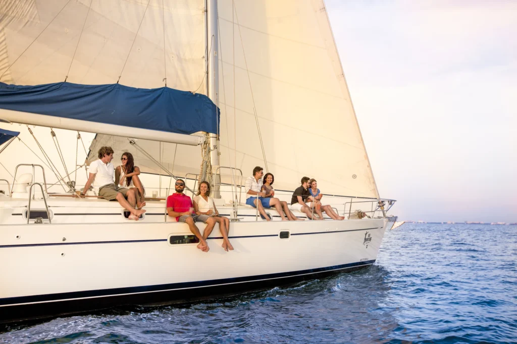 Guests sit in a line along the rail of a sailing boat with the sails up behind them.