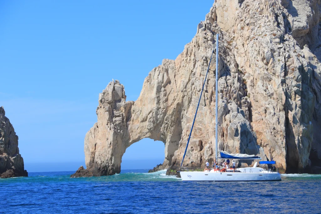 A sailing boat on blue water directly beside the Land’s End Arch.