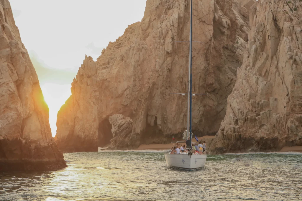 A sailing boat seen between two granite rocks with a sunburst above.